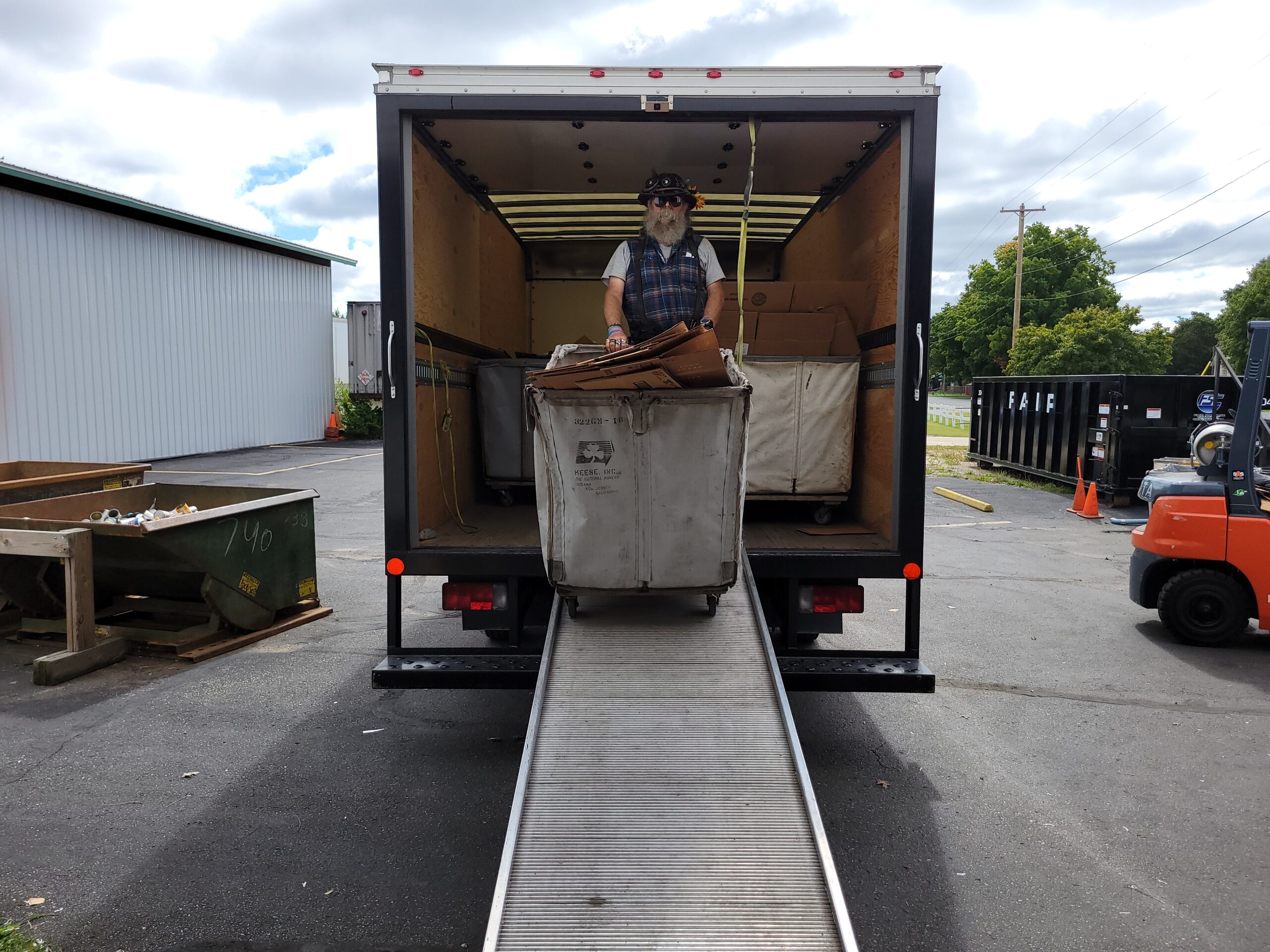 A man unloads a cart of recyclable materials from the back of a box truck.