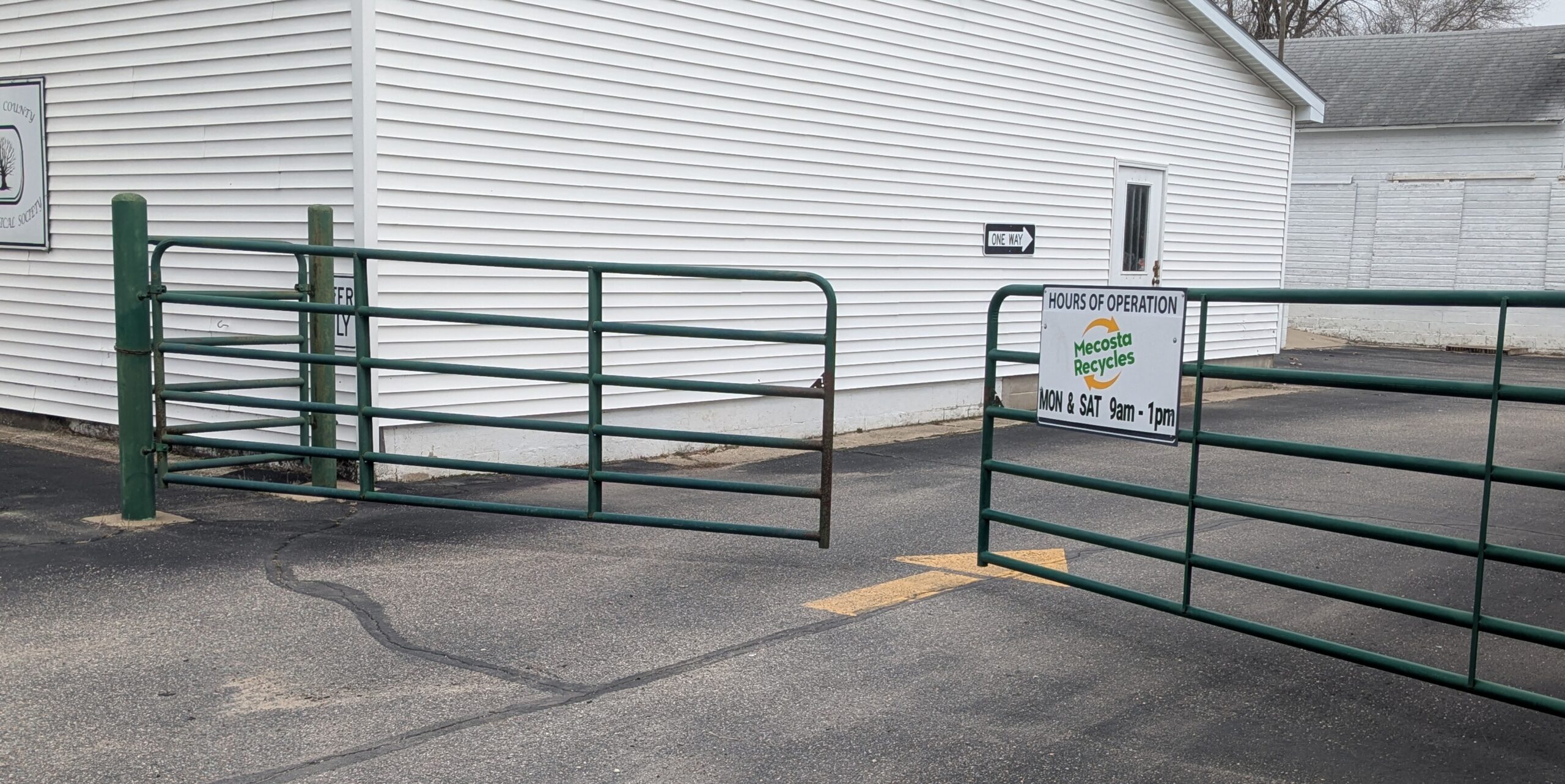 Entrance driveway to the recycling center. An arrow on the ground indicates the direction of traffic. A sign displays hours of operation: Mondays and Saturdays 9am to 1pm.